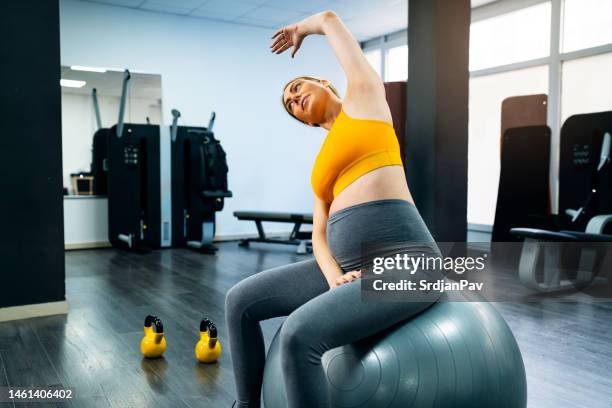 pregnant woman sitting on the fitness ball and stretching her body in the gym - fitness ball stock pictures, royalty-free photos & images