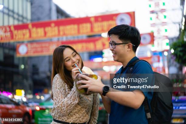 young thai couple enjoys drinking fresh coconut water while traveling in bangkok chinatown - 2 coconut drinks ストックフォトと画像