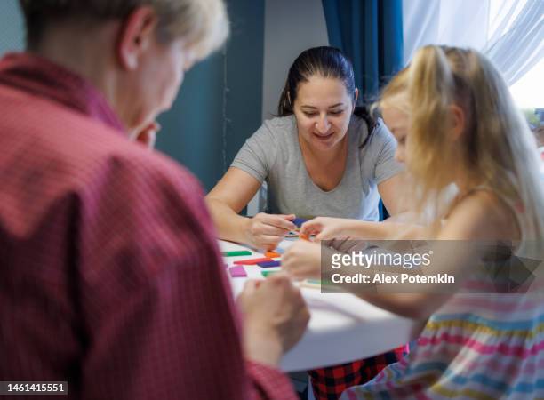 madre, figlia e nonna a tavola che giocano insieme con i puzzle tangram. - "alex potemkin" or "krakozawr" foto e immagini stock