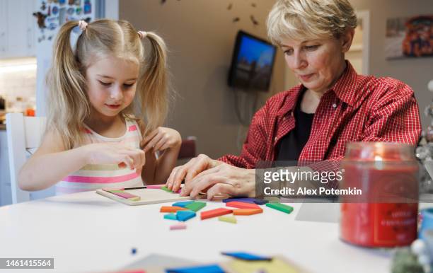 la bambina concentrata gioca con il puzzle tangram a tavola in cucina con sua nonna. - "alex potemkin" or "krakozawr" foto e immagini stock