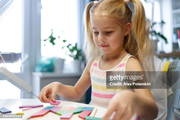ritratto di bambina sorridente felice che gioca con il puzzle tangram, con messa a fuoco superficiale - messa a fuoco selettiva sul suo viso. - "alex potemkin" or "krakozawr" foto e immagini stock