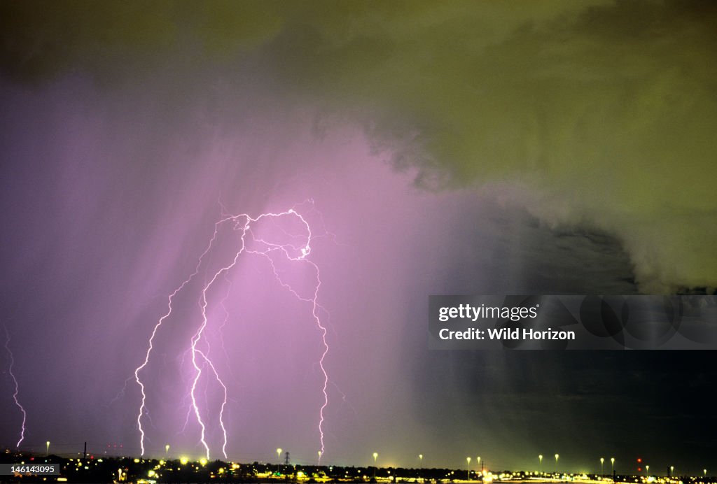 Active storm cell over city with scud clouds in foreground and a rain curtain behind, containing multiple cloud-to-ground lightning discharges Tucson, Arizona, USA