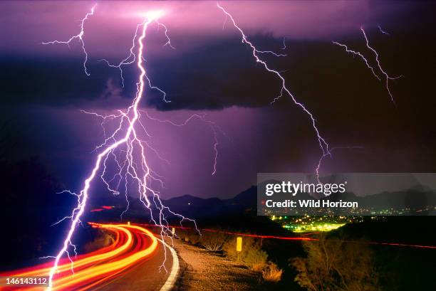 Sonoran Desert rainstorm, a summer monsoon thunderstorm with cloud-to-ground lightning strikes and light trails from cars on roadway, This image was...