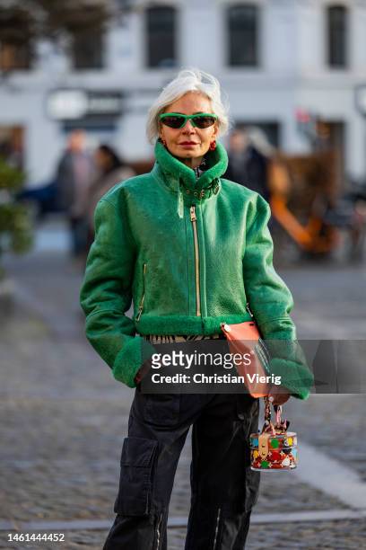 Grece Ghanem wears green shearling jacket, black flared pants with zipper, side pockets, orange clutch outside Lovechild 1979 during the Copenhagen...