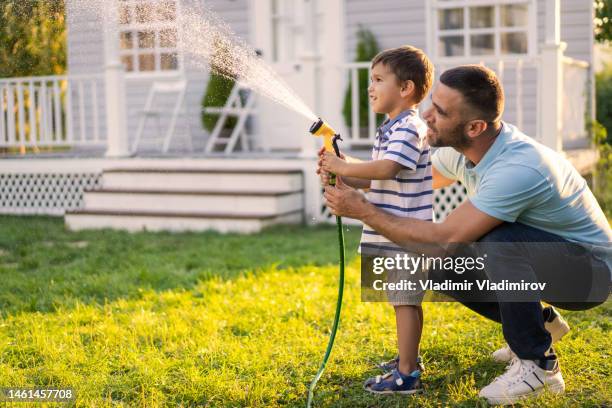 father and son are sprinkling the grass with water - tuinslang stockfoto's en -beelden