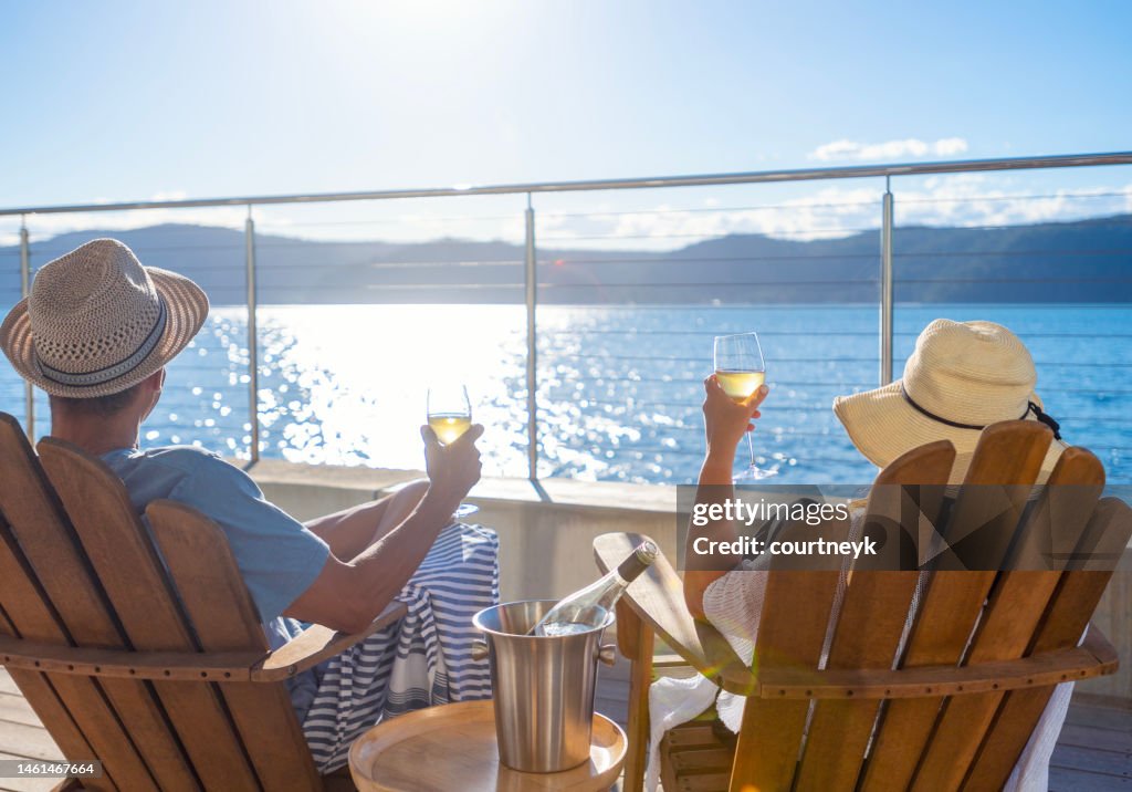 Couple relaxing and drinking wine on deck chairs in an over water bungalow.