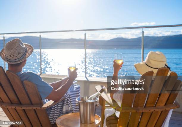 couple relaxing and drinking wine on deck chairs in an over water bungalow. - beach deck chairs stock pictures, royalty-free photos & images