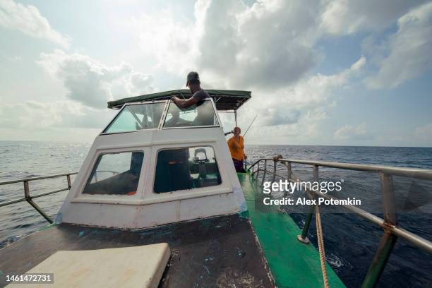 il capitano governa una piccola barca da pesca d'altura e un membro dell'equipaggio riposa in cima alla tuga quando il turista, donne europee, riposa sulla schiena. - "alex potemkin" or "krakozawr" foto e immagini stock