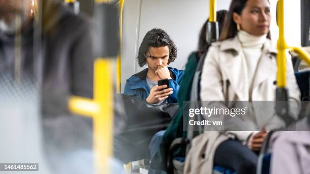 joven leyendo desde un teléfono inteligente en un autobús urbano - man riding bus fotografías e imágenes de stock