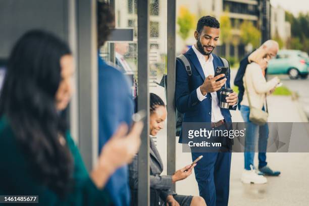 junger afroamerikanischer geschäftsmann chattet auf smartphone an bushaltestelle - alter mensch bushaltestelle stock-fotos und bilder