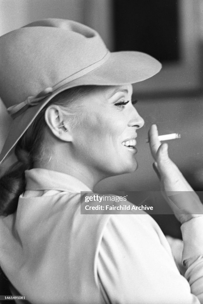 Portrait of American actress Faye Dunaway wearing a pale pearl gray shirt and vest in heavy silk crepe with awrapped mini-skirt in light gray linen, white stockings and beige alligator shoes, topped off with a felt slouch hat in lavender, a Theodora Van R
