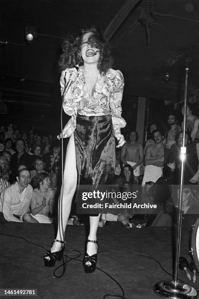 Actress and singer Bette Midler, wearing a velvet skirt and platform shoes, performing for a crowd of gay men at the Continental Club bath house in...