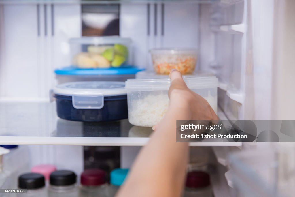 Asian woman stored leftovers food in plastic container put into refrigerator.