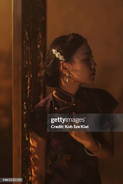 beautiful chinese woman in a qipao holding leaning towards a wooden divider in a studio portrait setting - chinese collar stock pictures, royalty-free photos & images