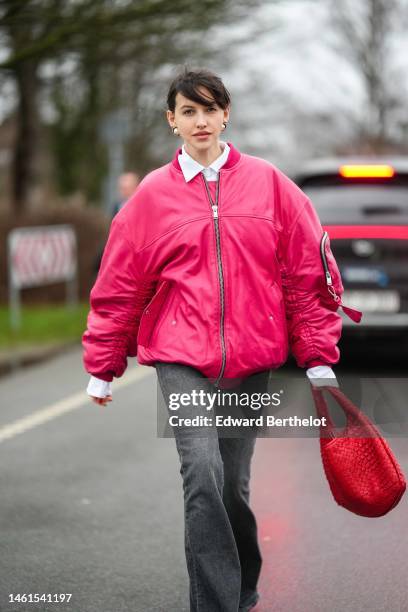 Guest wears gold and white large pearls earrings, a white shirt, a neon pink shiny leather oversized bomber coat, a red shiny leather braided...