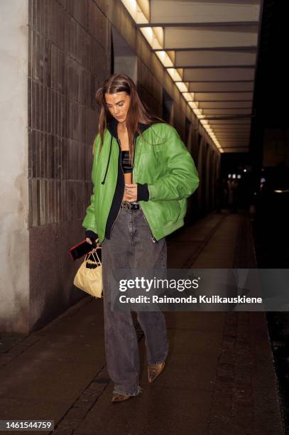 Guest wearing wide black jeans, black crop top, green leather jacket, pale yellow bag, and brown shoes outside Remain during the Copenhagen Fashion...