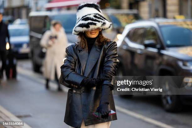 Guest wears black leather jacket, silk skirt, faux fur hat, gloves outside Skall Studio during the Copenhagen Fashion Week Autumn/Winter 2023 on...