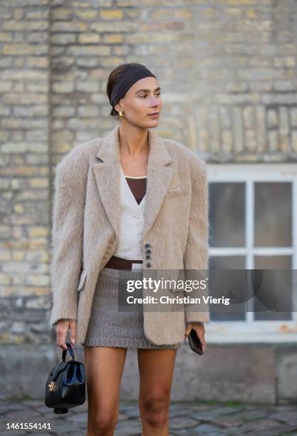 Vera van Erp wears beige jacket, mini skirt, vest, black mid high boots, white socks, black bag, head band outside Skall Studio during the Copenhagen...