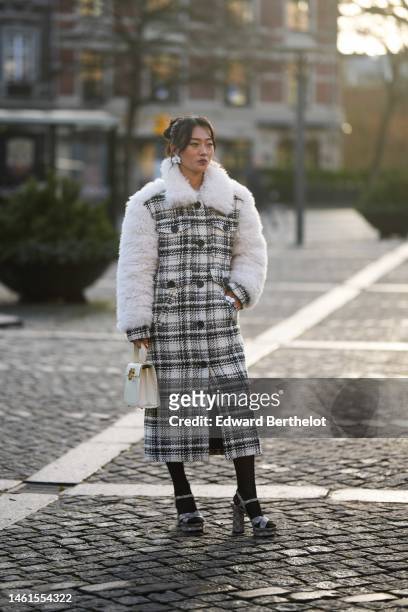 Guest wears silver large earrings, a black and white checkered tweed pattern with white oversized fluffy sheep collar and sleeves buttoned long coat,...