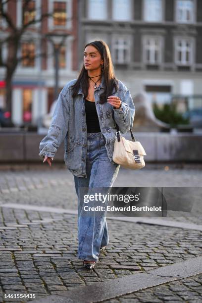 Guest wears a black headband, silver earrings, a black lace with silver pendant necklace, a blue faded denim oversized jacket, matching blue faded...