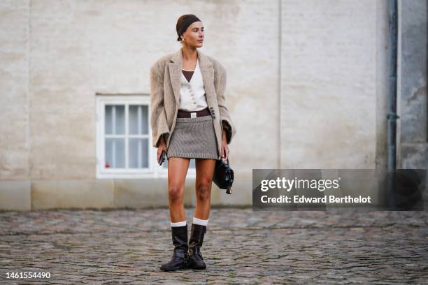 Guest wears a black headband, gold earrings, a brown tank-top, a white buttoned blazer jacket, a beige fluffy blazer jacket, a gray ribbed wool short...