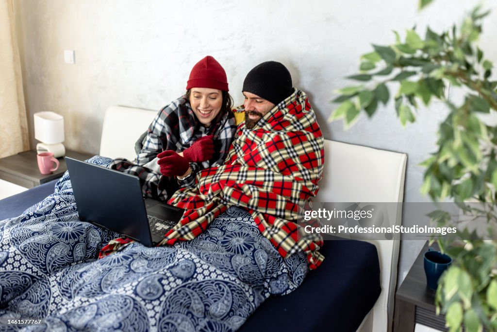 A young man and woman are feeling displeased due to the cold temperature in his apartment.
