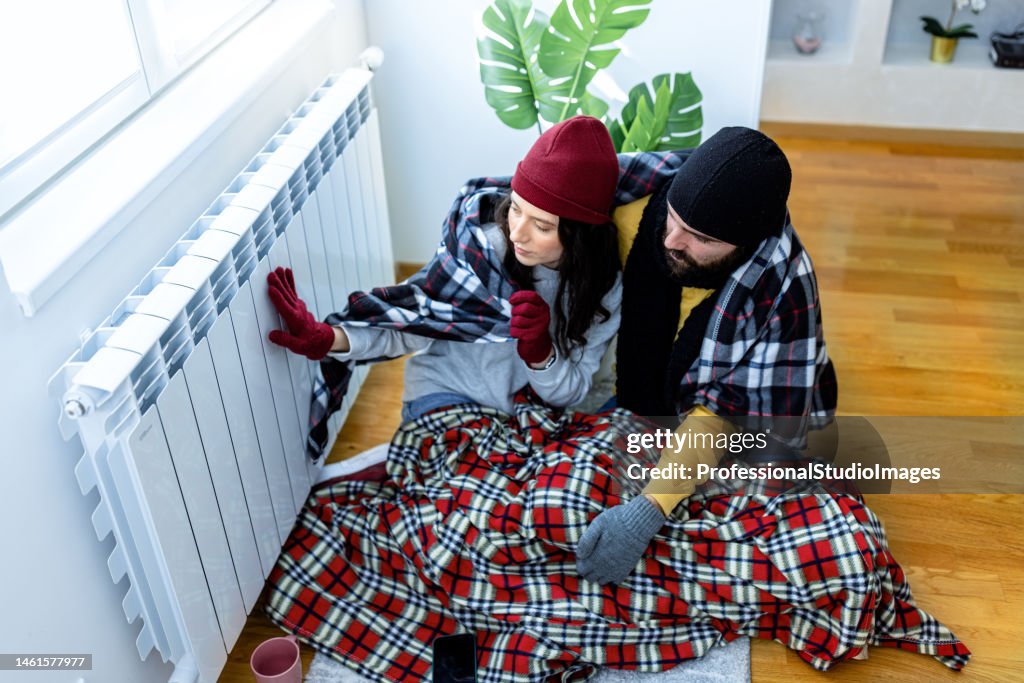 A young man and woman are feeling displeased due to the cold temperature in his apartment.