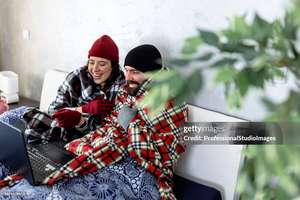 A young man and woman are feeling displeased due to the cold temperature in his apartment.