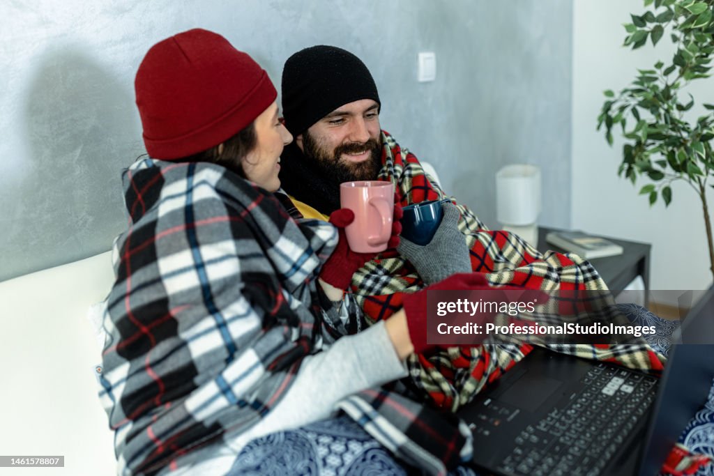 A young man and woman are feeling displeased due to the cold temperature in his apartment.