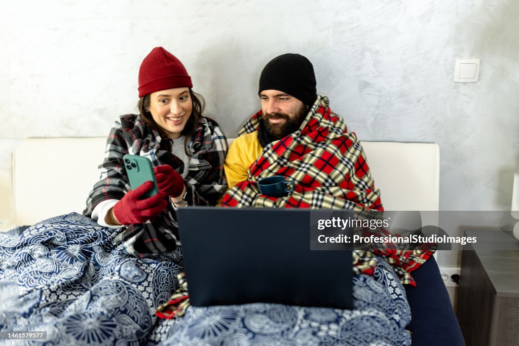 A young couple is suffering from a cold temperature during an energetic crisis and trying to warm up in a bedroom.
