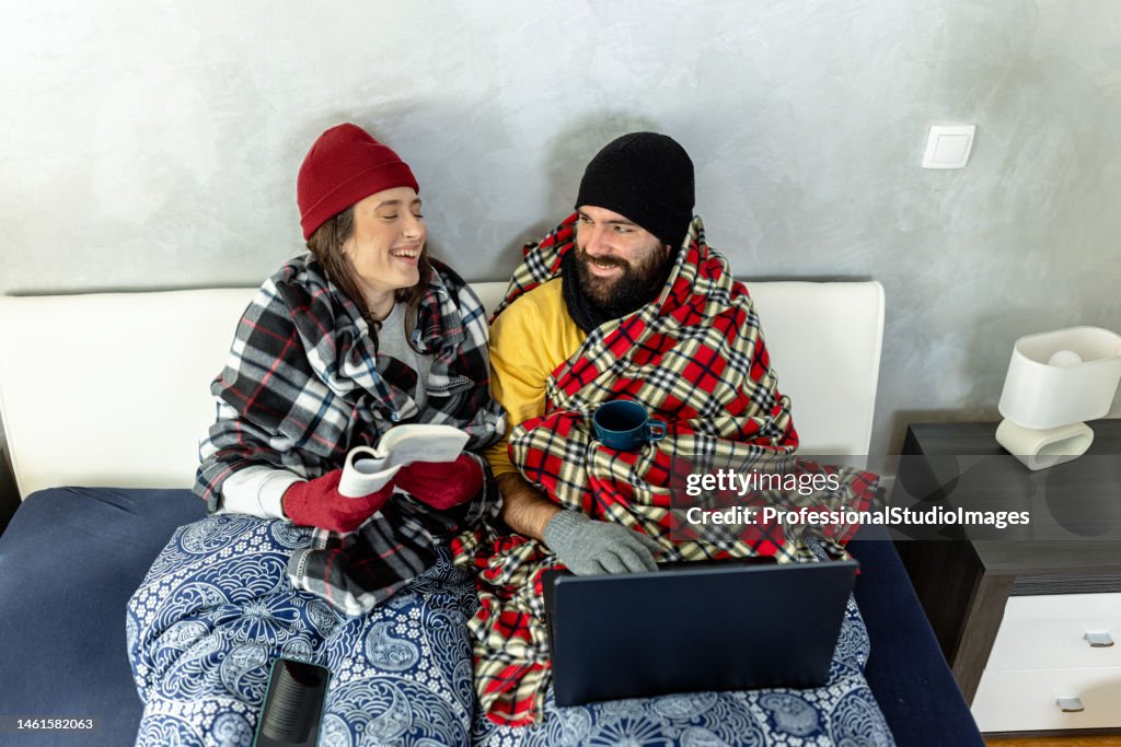 A young couple is suffering from a cold temperature during an energetic crisis and trying to warm up in a bedroom.