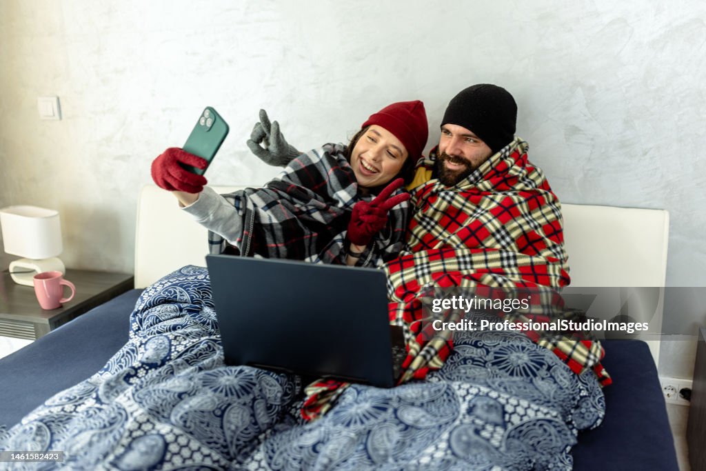 A young couple is suffering from a cold temperature during an energetic crisis and trying to warm up in a bedroom.