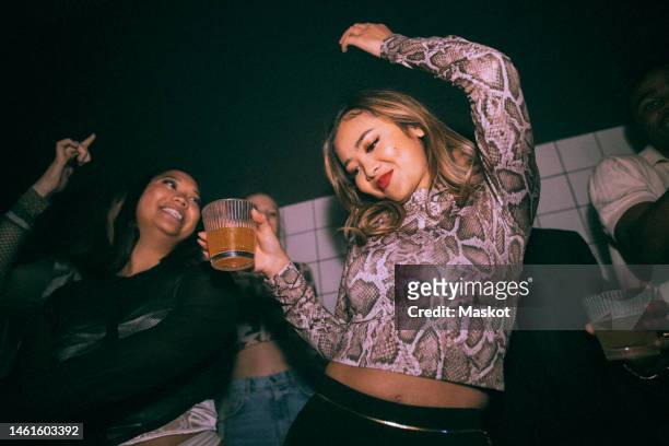 carefree young woman with drink dancing by female friend enjoying at nightclub - using a swing stockfoto's en -beelden