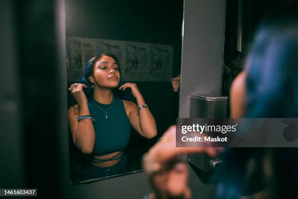 reflection of young woman looking at mirror reflection in nightclub bathroom - bathroom mirror fotografías e imágenes de stock