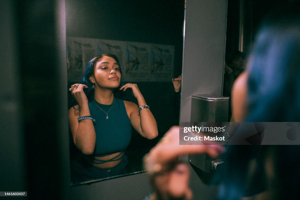 Reflection of young woman looking at mirror reflection in nightclub bathroom