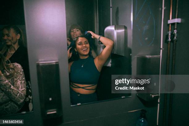 happy young woman enjoying with friends while looking at mirror reflection in nightclub bathroom - nightclub bathroom stock pictures, royalty-free photos & images