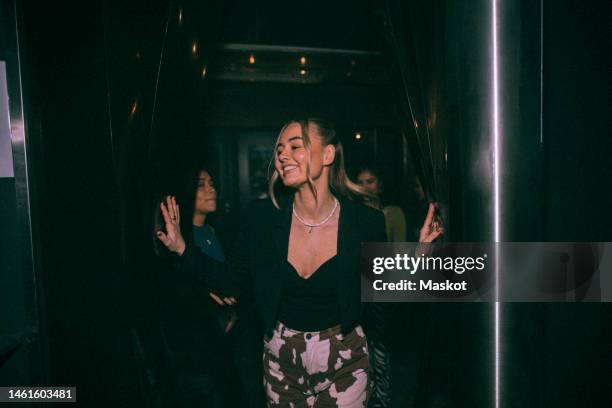 cheerful young woman getting out of bathroom with friends in background at nightclub - nightclub bathroom stock pictures, royalty-free photos & images