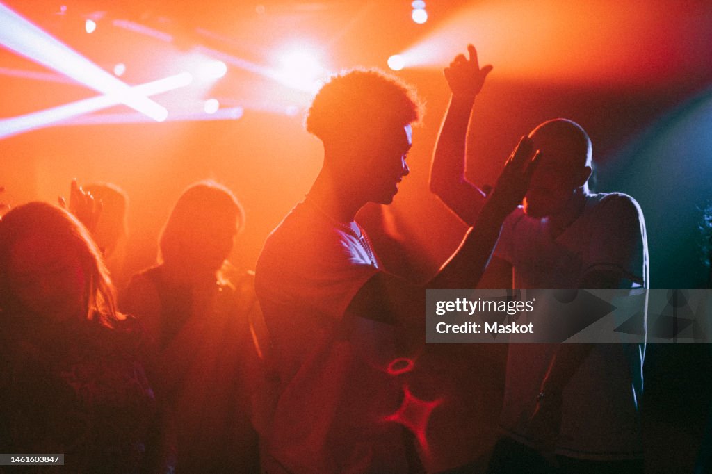 Young men and women dancing against illuminated red spotlights at nightclub
