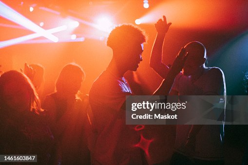 Young men and women dancing against illuminated red spotlights at nightclub Young men and women dancing against illuminated red spotlights at nightclub