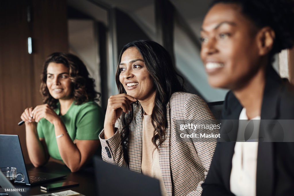 Smiling mature businesswoman with hand on chin planning strategy with colleagues at office