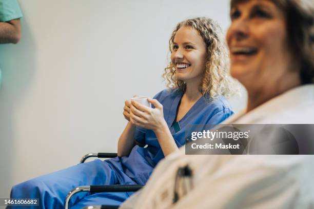 happy female nurse holding coffee cup while sitting on chair by colleague - nurse resting stock pictures, royalty-free photos & images