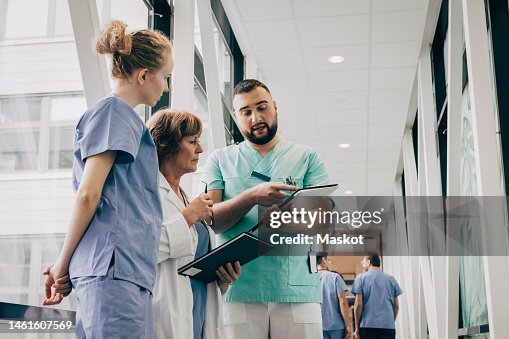 Male healthcare worker explaining over clipboard to doctor at hospital