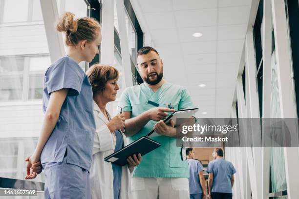 male healthcare worker explaining over clipboard to doctor at hospital - profissional da área médica imagens e fotografias de stock