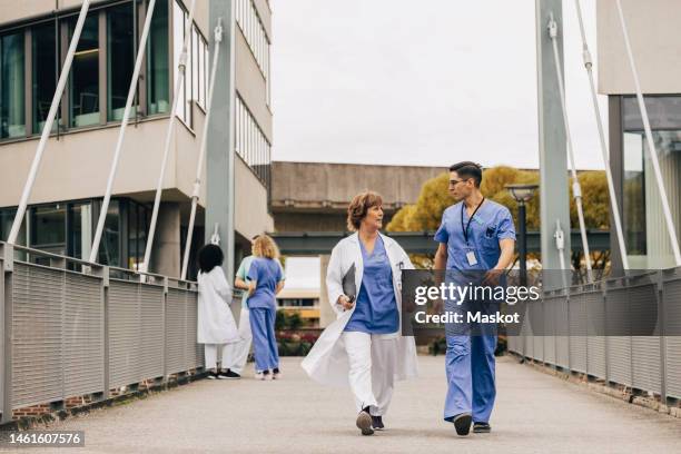 female doctor talking while walking with hospital staff on bridge - hospital exterior stock pictures, royalty-free photos & images