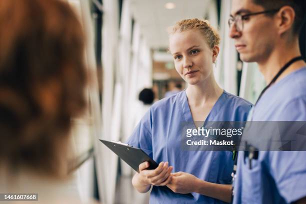 young female hospital staff holding clipboard while discussing with colleagues - hospital staff 個照片及圖片檔