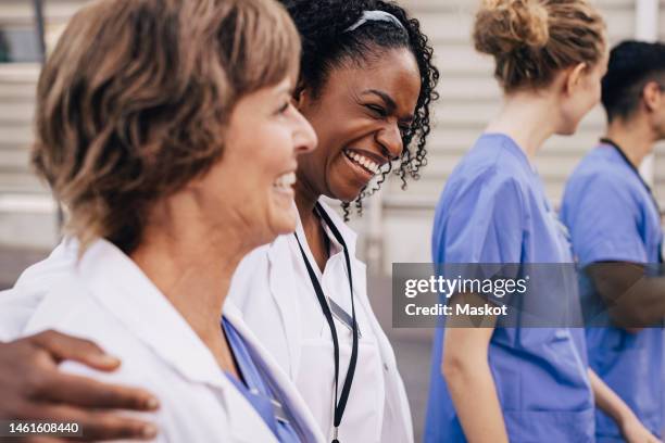 happy female physician with arm around colleague outside hospital - medical imagens e fotografias de stock