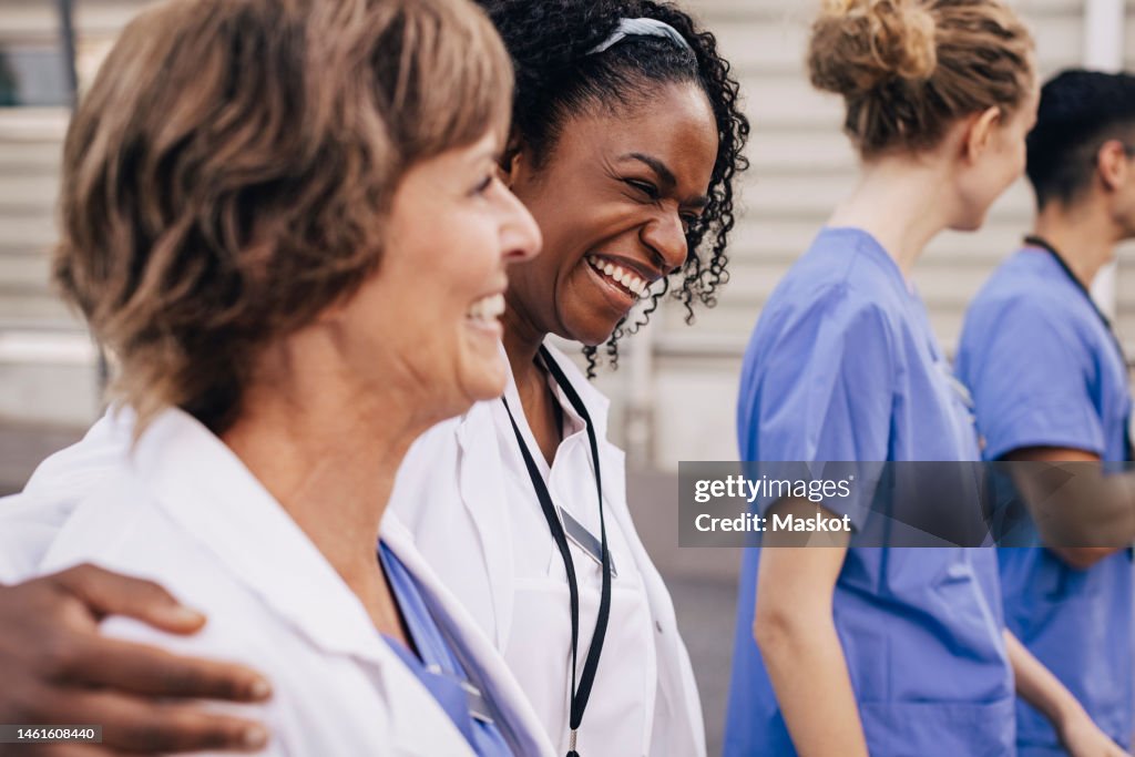 Happy female physician with arm around colleague outside hospital