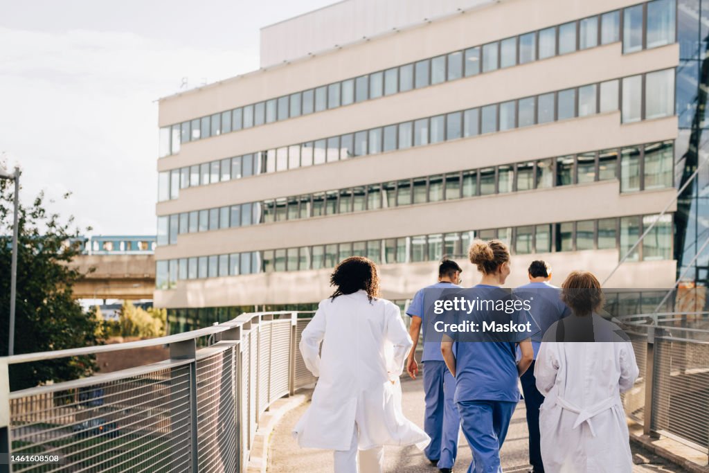 Male and female healthcare professional walking on bridge leading towards hospital