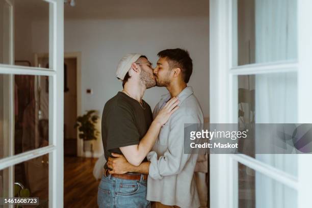 side view of romantic gay couple kissing each other seen through doorway - gay kiss stock-fotos und bilder