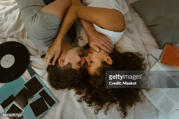 directly above view of romantic couple rubbing noses while lying on bed at home - couple in bed fotografías e imágenes de stock